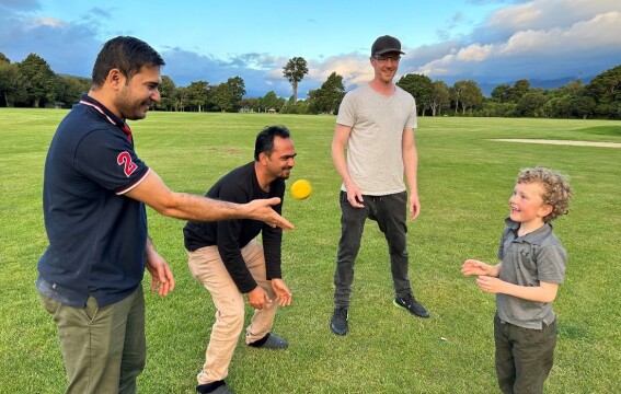 Three men playing cricket with a child. 