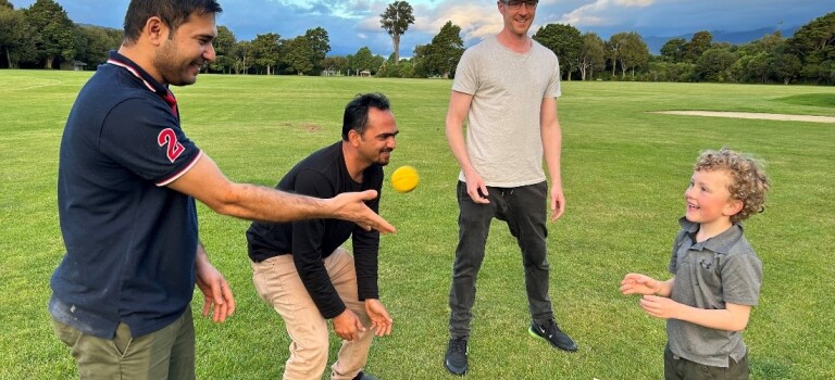 Three men playing cricket with a child. 