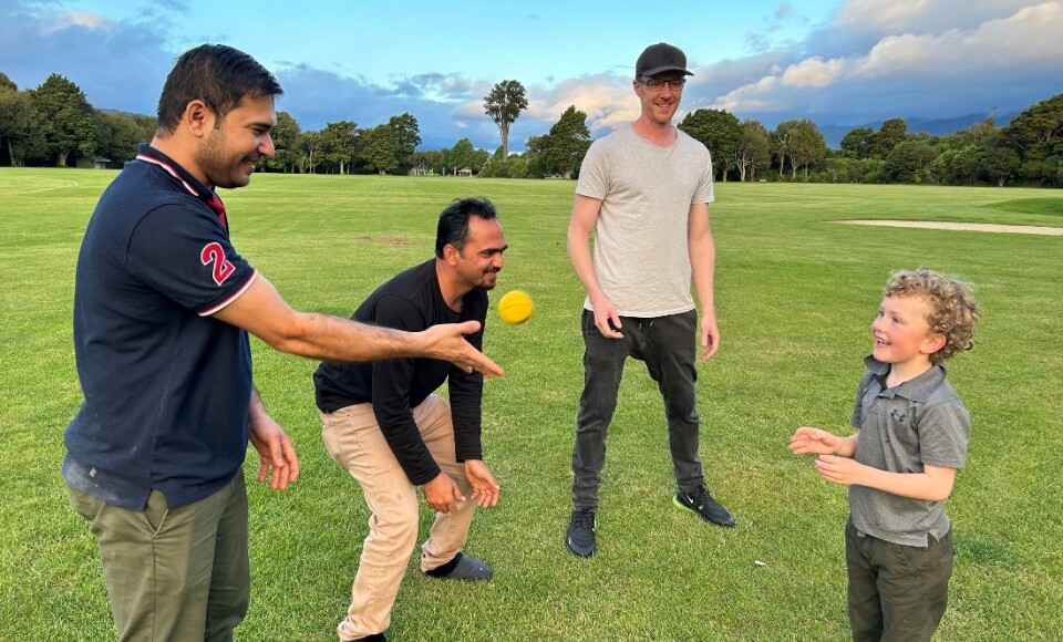 Three men playing cricket with a child. 