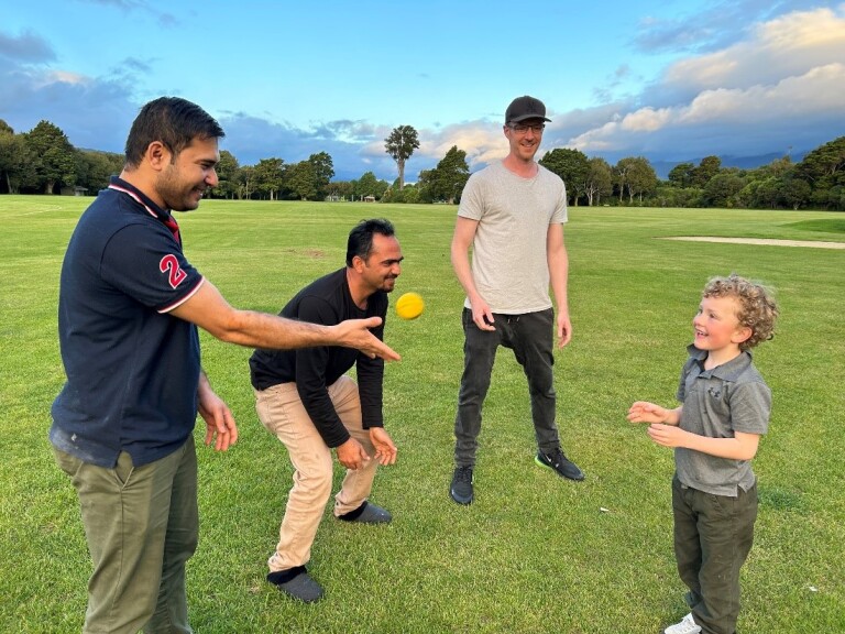 Three men playing cricket with a child. 