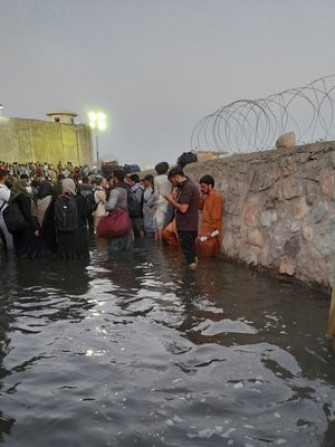 A large group of people huddled near a wall standing in knee-deep water. 