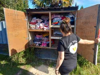 Photo of Lynsey Abbott from One Voice Charitable Trust with the pataka kai (pantry) she has outside her house, with free food for those in the community that need it.