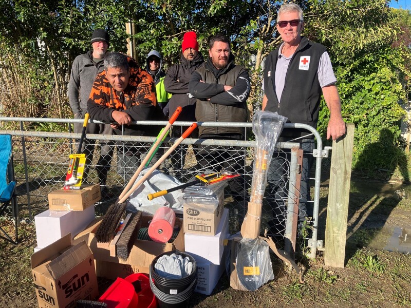 A group of men standing behind a pile of clean-up equipment such as brooms and buckets. 