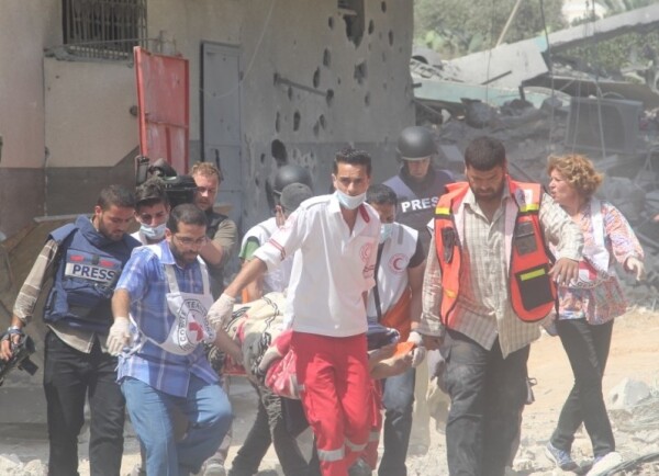 A group of medical workers and press carrying a wounded person on a stretcher