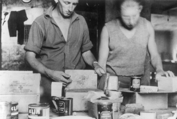Two men opening boxes of tinned goods