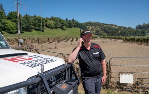 A man standing next to a vehicle using a satellite phone 