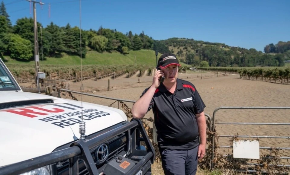 A man standing next to a vehicle using a satellite phone
