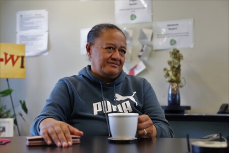 A woman sits at a table drinking a cup of coffee.