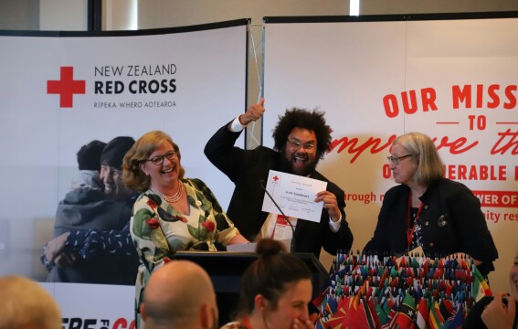 A smiling man holding a certificate, two women on either side of him are smiling and laughing