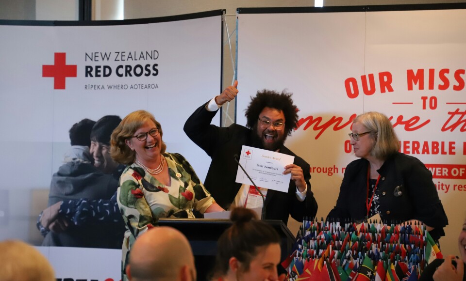 A smiling man holding a certificate, two women on either side of him are smiling and laughing