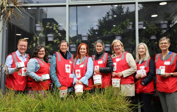 A group of people standing in a line looking at the camera. They're all wearing fundraising bibs and carrying donation buckets. 