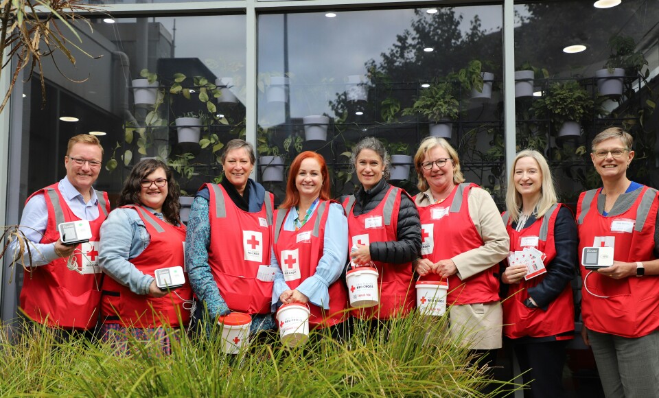 A group of people standing in a line looking at the camera. They're all wearing fundraising bibs and carrying donation buckets. 