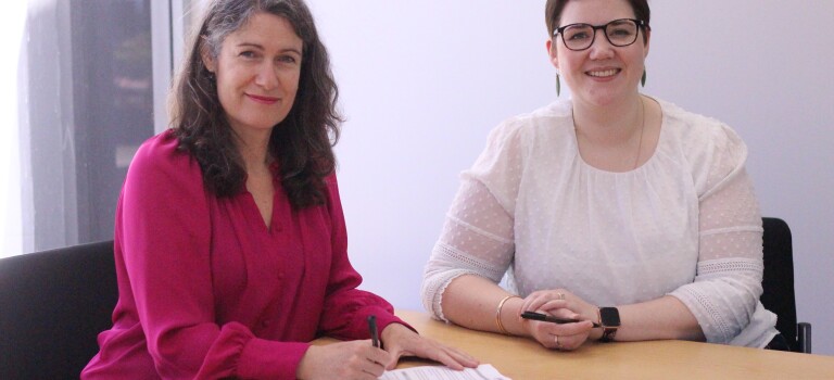 Two women sitting together signing a document