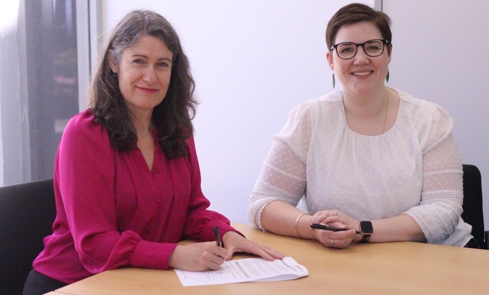 Two women sitting together signing a document