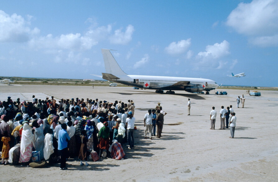 A large group of people on a tarmac with an aircraft in the background.