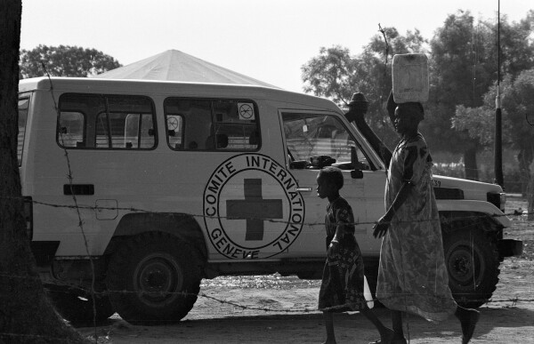 A woman and a child carrying water next to an ICRC vehicle.