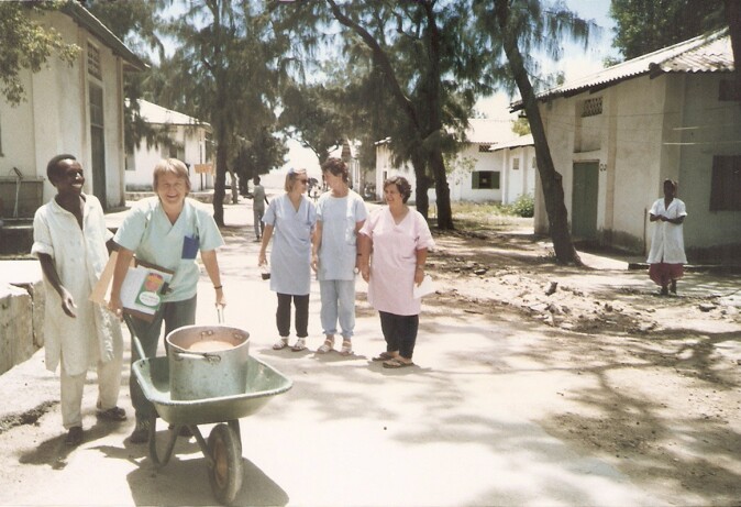 A woman carrying a wheelbarrow with a group of people next to her.