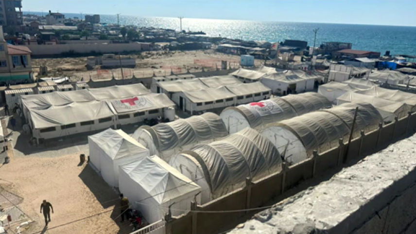A group of tents arranged in a row, set against an open sky and near the ocean. The scene is outdoors, with the tents positioned on the concrete base.