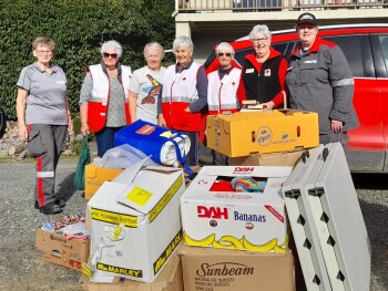 A group of seven women is standing in front of boxes of goods
