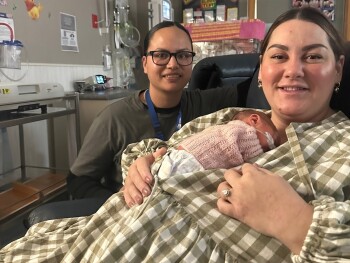 A women sitting in a chair holding a baby and another women in the background