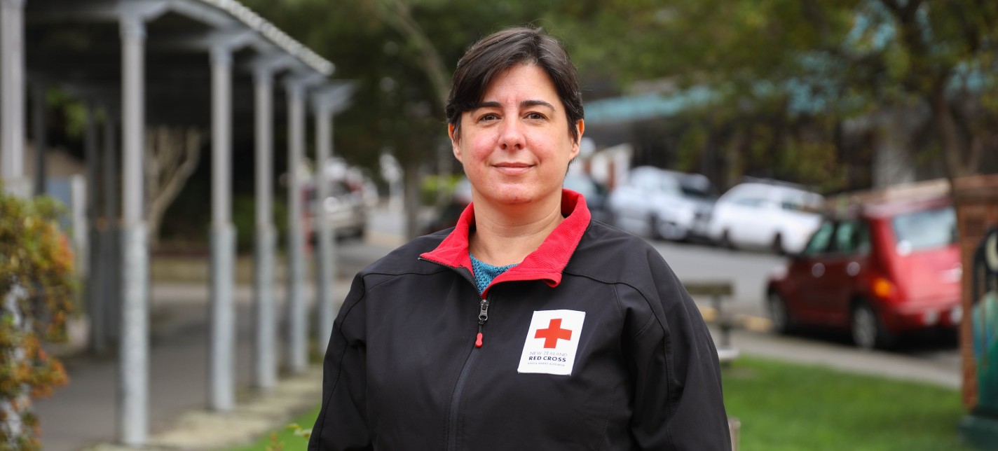 A Red Cross volunteer standing in a garden with red flowers behind her