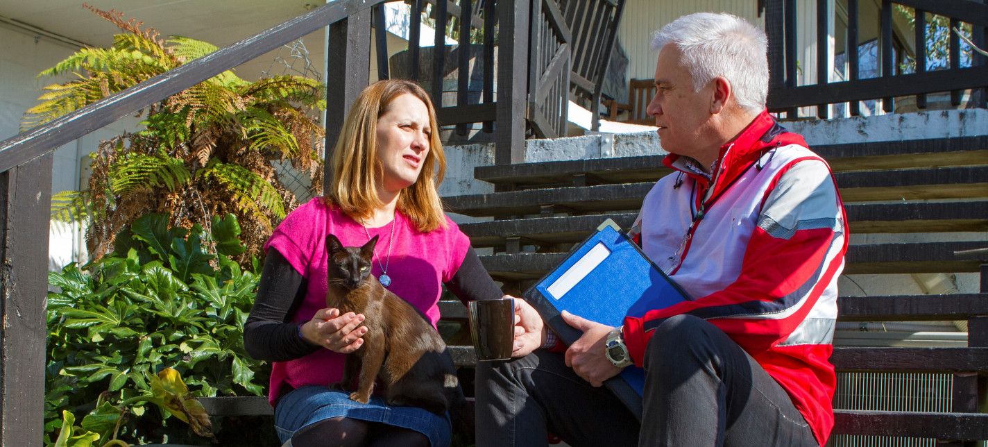 A woman holding a cat sits next to a man on some steps