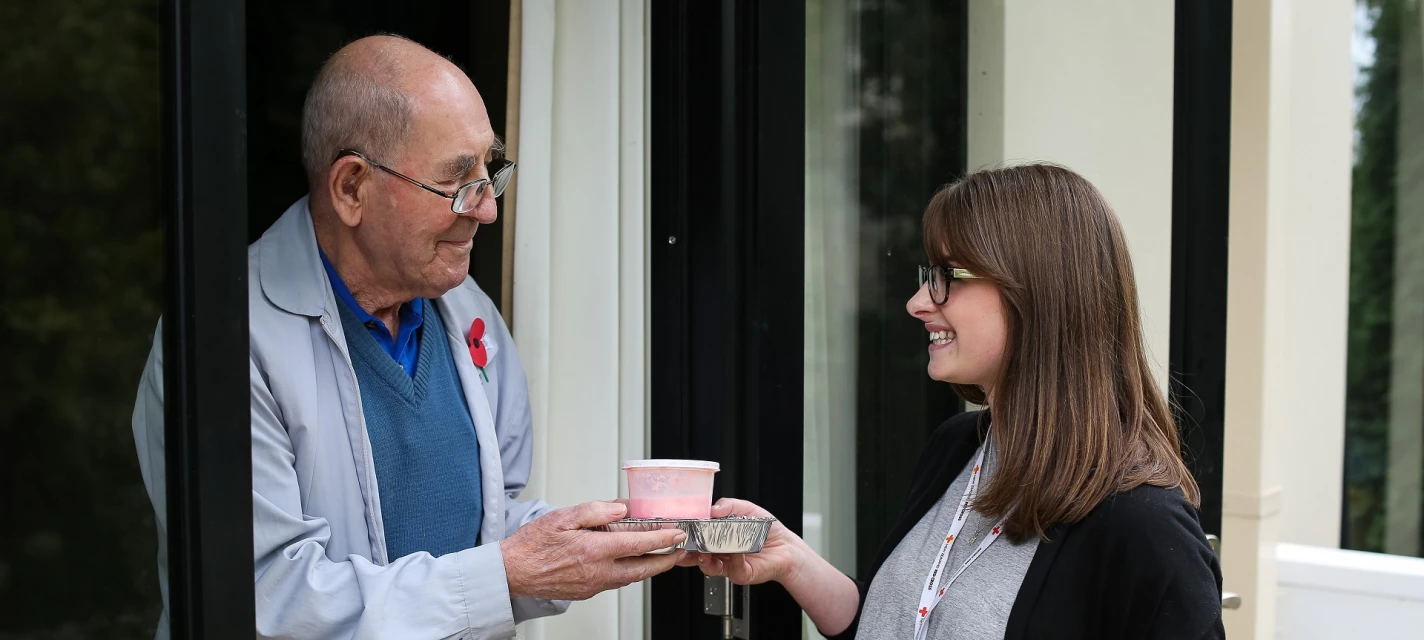 A woman handing a man a packaged meal.