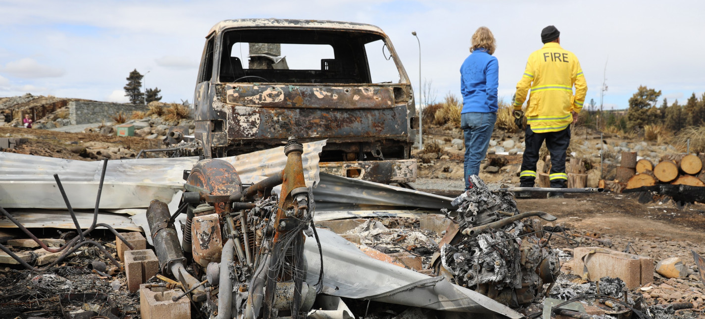 People standing next to a destroyed vehicle.