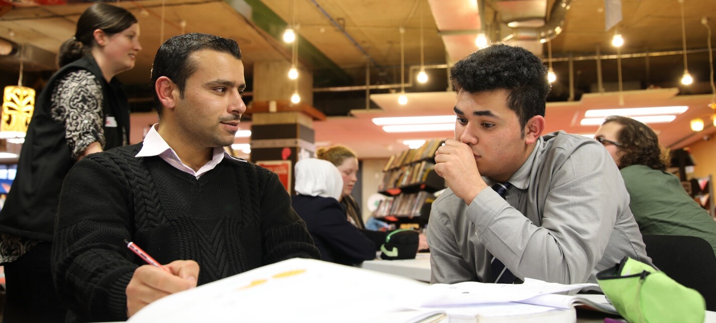 Two men working at a desk with books spread out in front of them