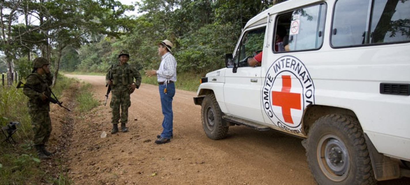 A Red Cross volunteer stands talking to two soldiers on the road by his vehicle