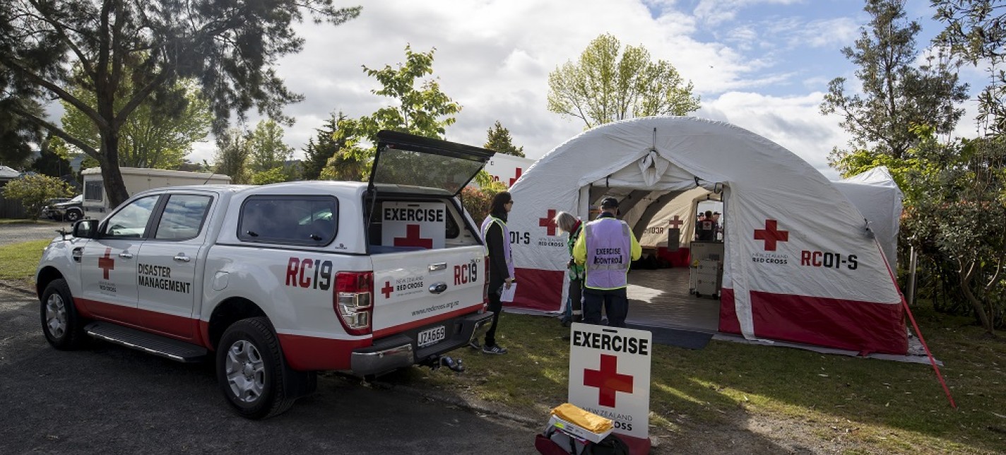 A Red Cross vehicle parked next to a Red Cross tent in a park