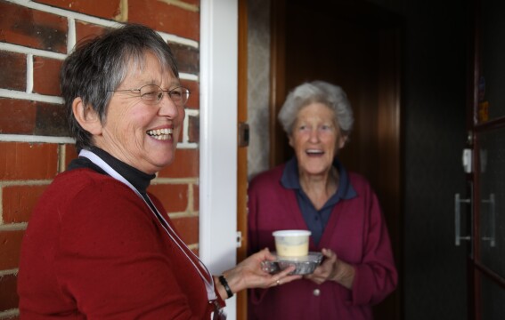 A woman giving another woman a packaged meal. 