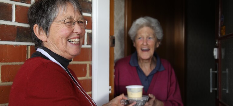 A woman giving another woman a packaged meal. 