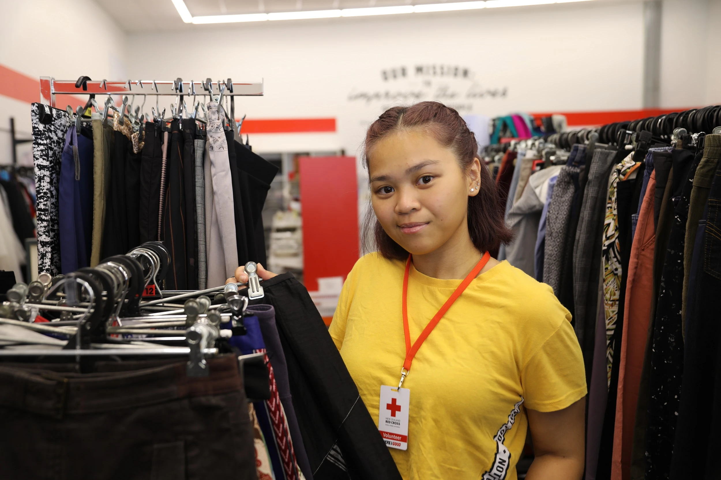 A volunteer stands by a rail of clothes in the Red Cross shop