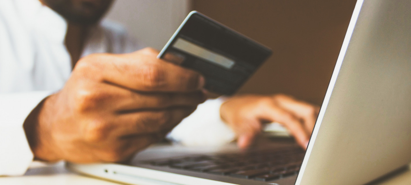 A man holds a credit card in one hand while typing on a laptop with the other