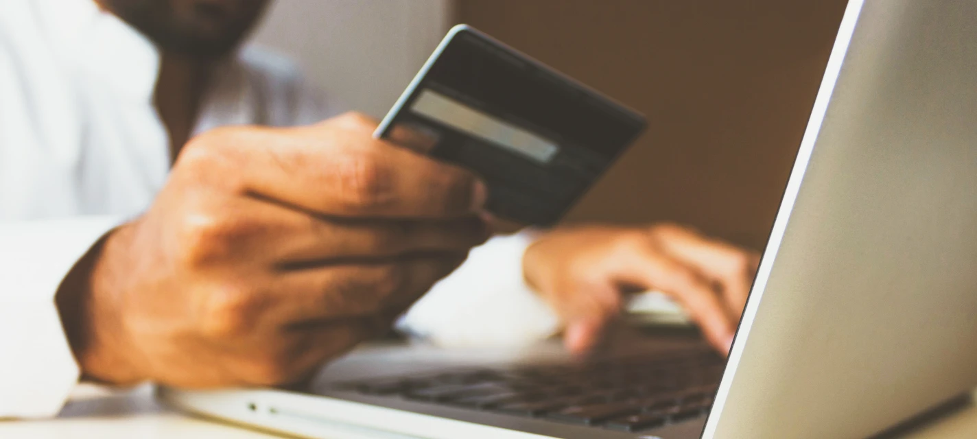 A man holds a credit card in one hand while typing on a laptop with the other
