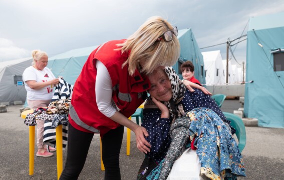HD hero image of Red Cross worker supports woman in emergency shelter