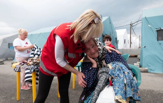 HD hero image of Red Cross worker supports woman in emergency shelter