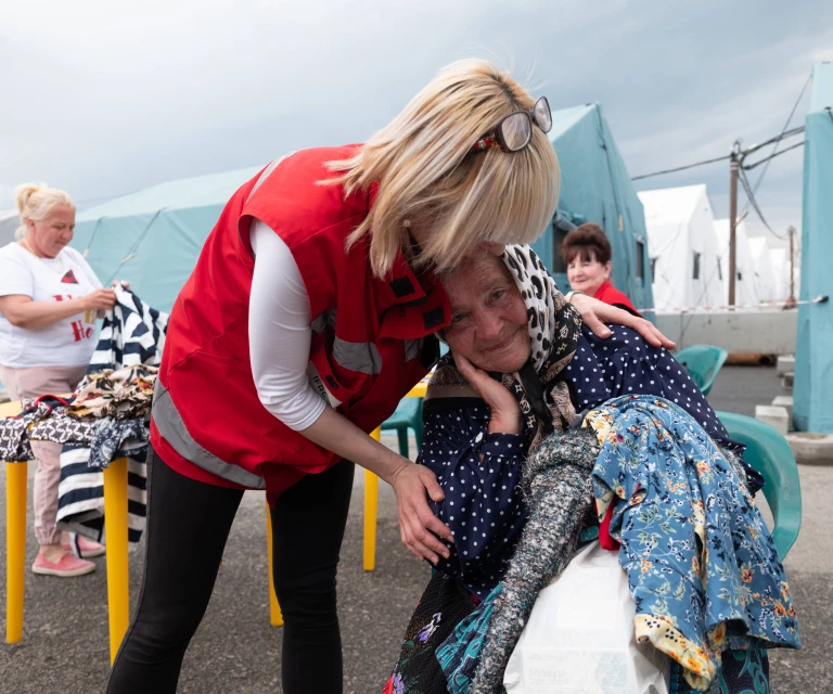 HD hero image of Red Cross worker supports woman in emergency shelter