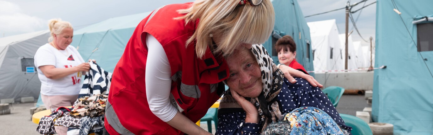 HD hero image of Red Cross worker supports woman in emergency shelter