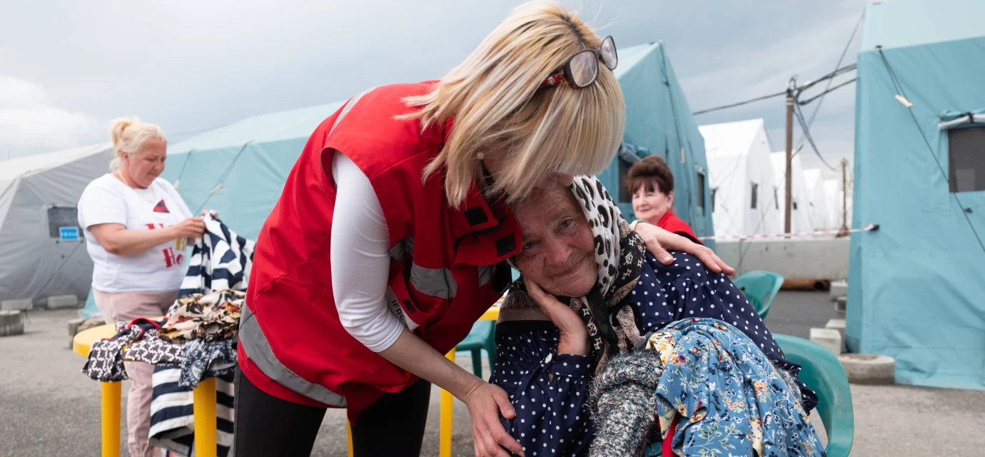 HD hero image of Red Cross worker supports woman in emergency shelter