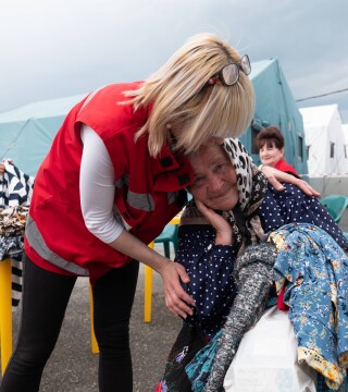 HD hero image of Red Cross worker supports woman in emergency shelter