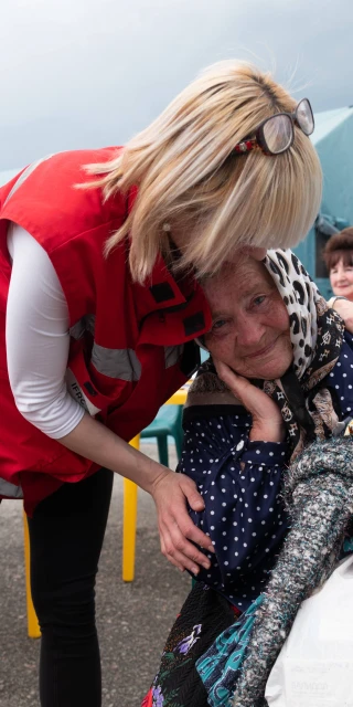 HD hero image of Red Cross worker supports woman in emergency shelter