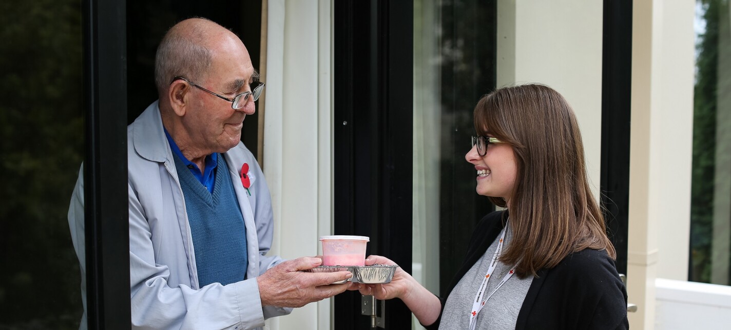 A woman handing a man a packaged meal.